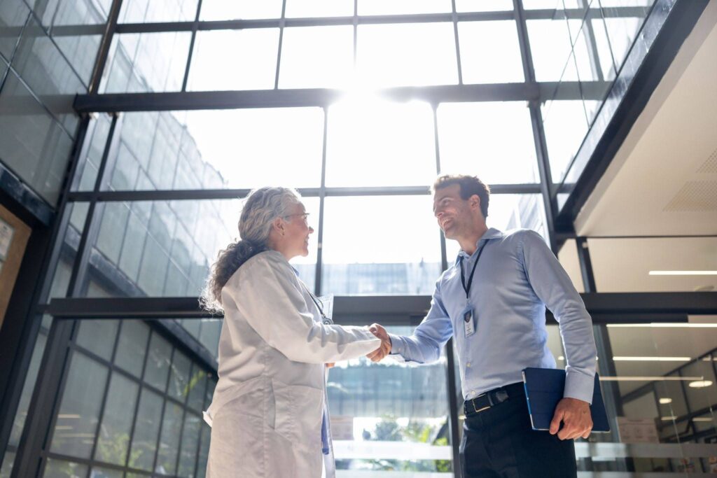 Two professionals shake hands in a bright, modern building atrium.