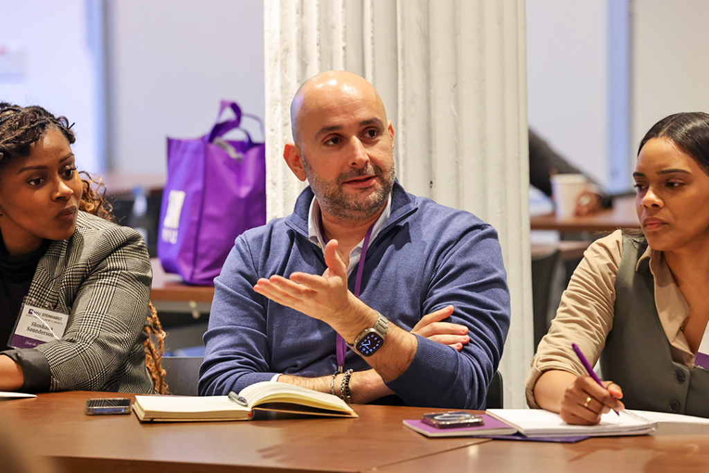 A man speaks and gestures during a meeting with colleagues at a table.