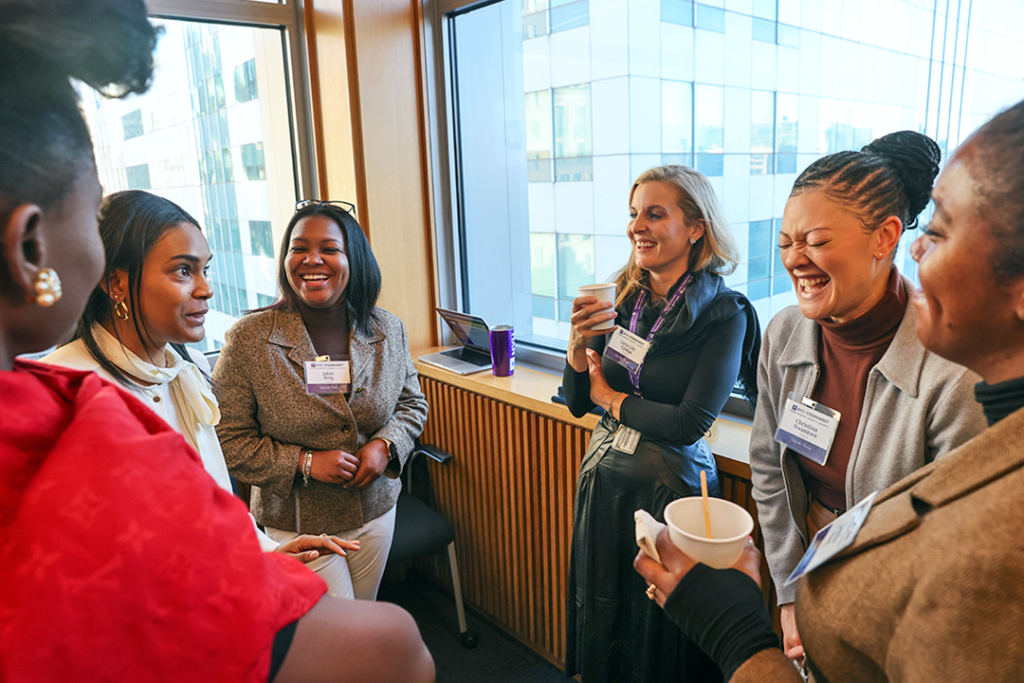 A group of NYU graduate students smile and laugh in conversation with each other.